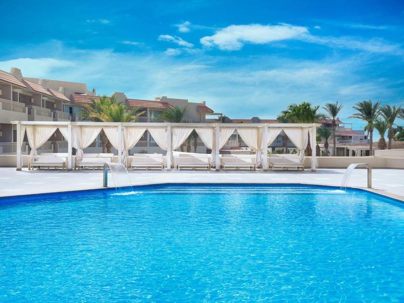 Resort pool with cabanas and a clear blue sky in the background.