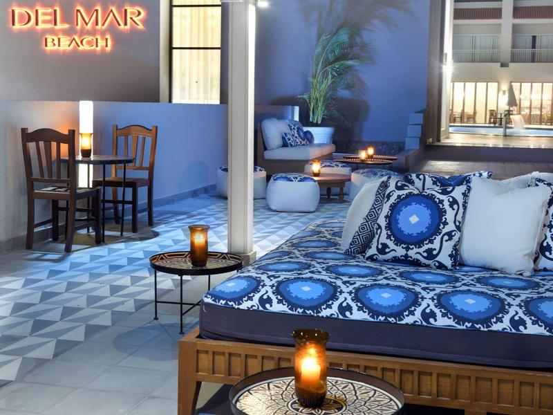 Cozy outdoor lounge with blue cushions, tiled floor, and warm candlelight near a bar area.