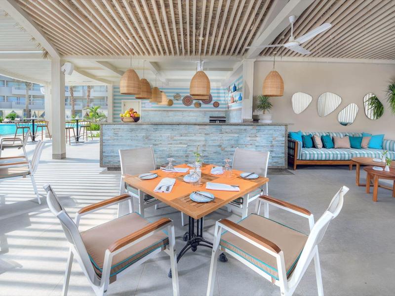 Bright hotel restaurant with modern wooden furniture and large windows overlooking the pool area.