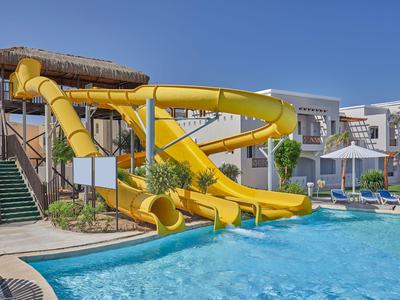 Gelbe Wasserrutsche neben Hotelpool mit Liegestühlen und Sonnenschirmen unter blauem Himmel.