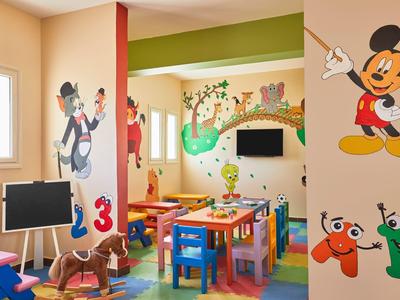 Buntes Kinderzimmer mit Mickey-Mouse-Wandbildern, Tischen, Stühlen und Spielzeugpferd.