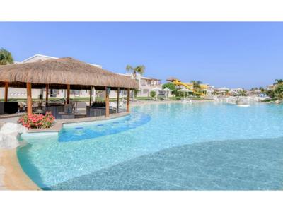 Großer Pool mit Swim-up-Bar und umliegenden Hotels unter klarem Himmel.