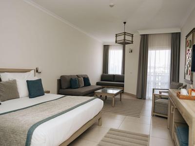 Moderne hotelkamer met groot bed, bank, bureau en balkon met gordijnen.