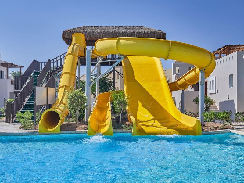 Žluté skluzavky a čistý bazén v hotelovém komplexu pod modrou oblohou.