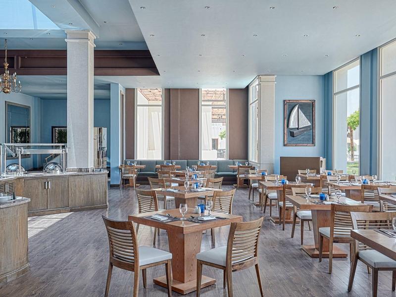 Prostorná světlá restaurace s dřevěnými stoly a židlemi u velkých oken.