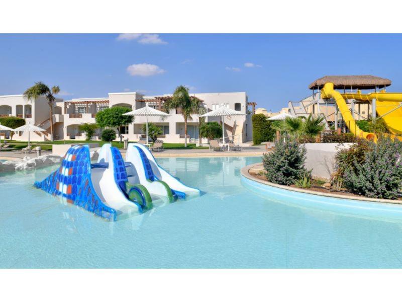 Hotelový bazén s barevnými skluzavkami za slunečného počasí a s vegetací.