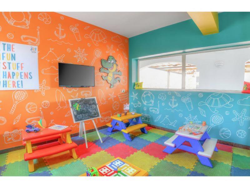 Barevná dětská herna se stoly, tabulí a televizí.