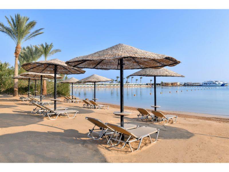 Lehátka a slaměné slunečníky na písečné pláži u klidného moře.