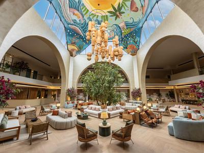 Ampia lounge dell'hotel con comodi posti a sedere, albero centrale e soffitto dipinto.