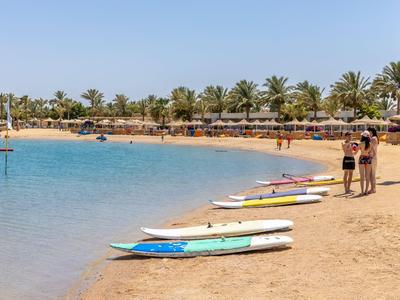 Strand mit ruhigem Wasser, mehreren Surfboards und zwei Personen in Badebekleidung.