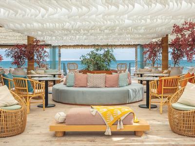 Vzdušný salón s ratanovým nábytkem, pohodlnými polštáři a výhledem na moře.