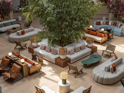 Pohodlná venkovní posezení s pohovkami, polštáři a velkým stromem uprostřed.