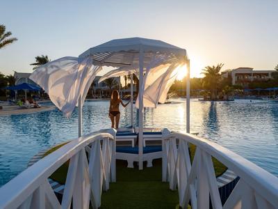 Zonsondergang bij hotelzwembad met paviljoen bereikbaar via een brug.