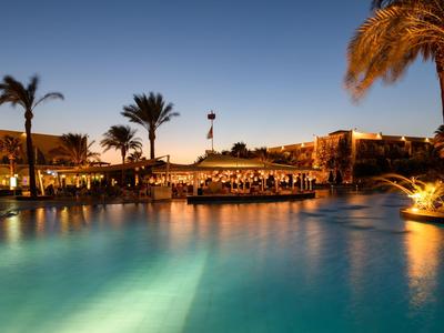 Beleuchteter Hotelpool umgeben von Palmen bei Sonnenuntergang.