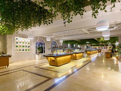 Lichte, moderne buffetruimte met decoratieve plafonds en veel groen in een hotel.