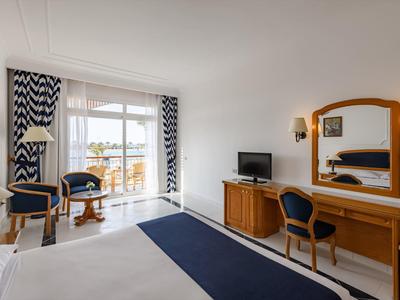 Lichte hotelkamer met balkon, tweepersoonsbed, bureau, tv en blauw-wit kleurenpalet.