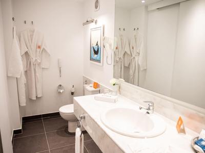 Moderne badkamer met wastafel, spiegel, toilet en meerdere badjassen aan de muur.