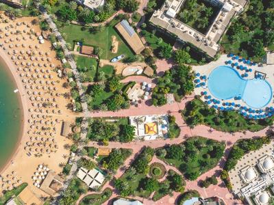 Luftaufnahme eines Resorts mit Strand, Pool und angrenzenden Gebäuden in einer grünen Umgebung.