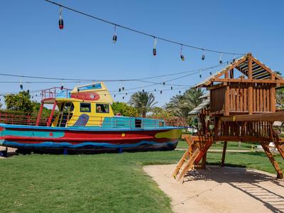 Kleurrijke speeltuin met een boot en houten boomhut op grasgrond.