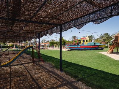 Overdekt gebied met hangmatten en speeltuin met schip op de achtergrond.