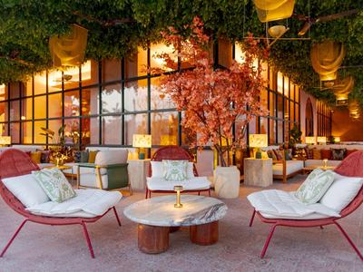 Gemütlicher Außenbereich mit roten Sesseln, Holztischen und warmem Licht in einem Hotelgarten.