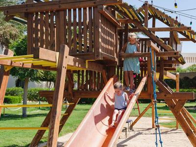 Kinderen spelen op een houten speelplaats met glijbaan in de tuin van een hotel.