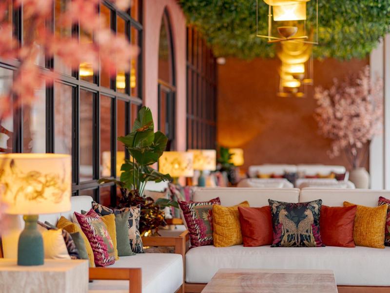 Gezellige lounge met banken en kleurrijke kussens, warme verlichting en decoratieve planten.