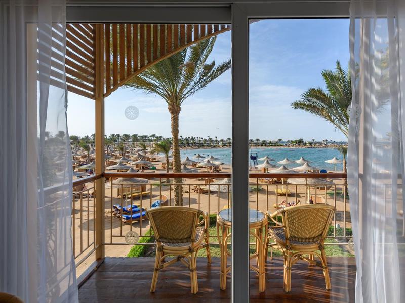 Balkon met twee stoelen en tafel met uitzicht op strand en palmbomen bij helder weer.