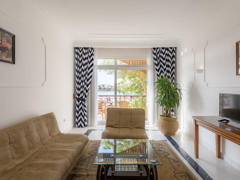 Lichte woonkamer met bruine bank, fauteuil, glazen tafel en balkon met plantenzicht.