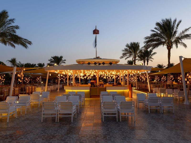 Avondzicht op een open strandrestaurant met palmbomen en lichtjes.