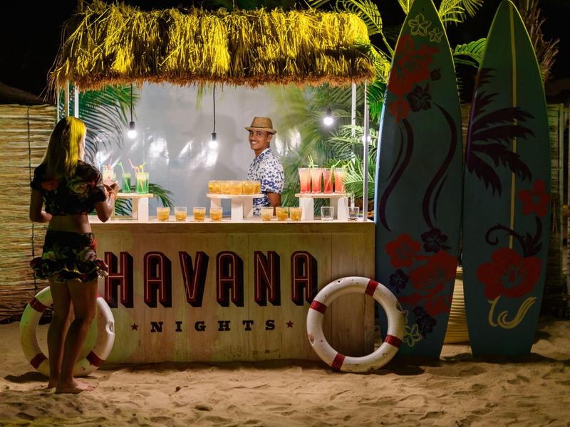 Strandbar met rieten dak 's nachts, barman achter de toonbank, surfplanken en reddingsboei zichtbaar