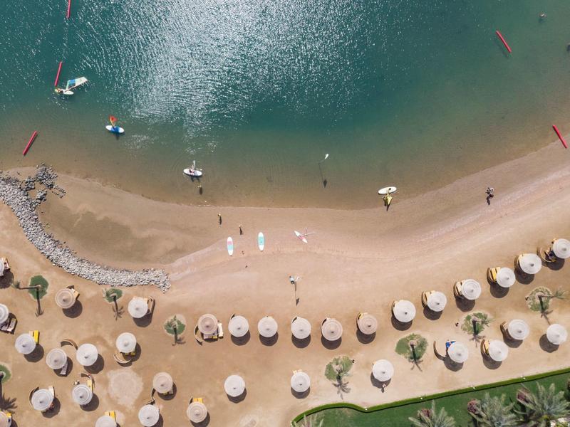 Luchtfoto van een strand met parasols, helder water en zand, gasten ontspannen aan de kust.
