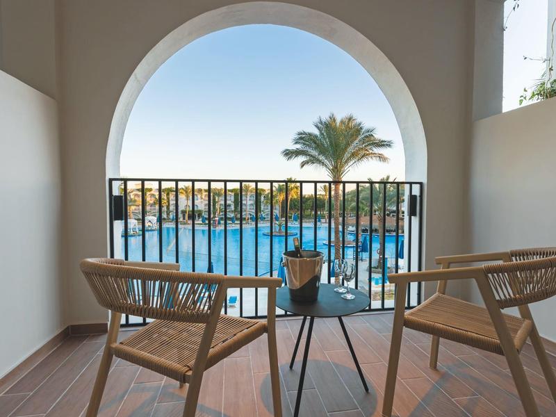 Balkon met twee stoelen en tafel met uitzicht op zwembad en palmboom.