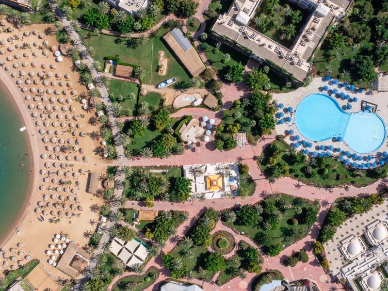 Luchtfoto van een hotel met groot zwembad en strand met ligbedden aan zee.