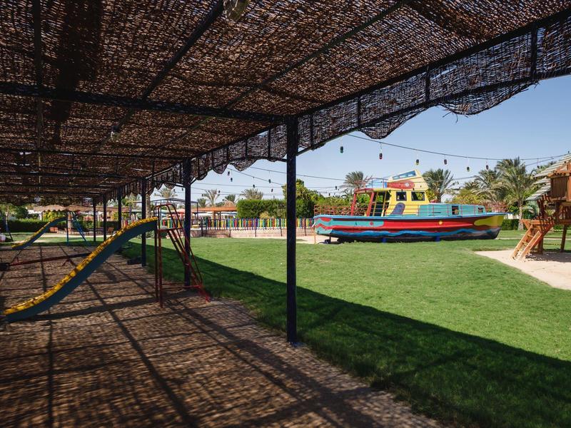 Overdekt gebied met hangmatten en speeltuin met schip op de achtergrond.