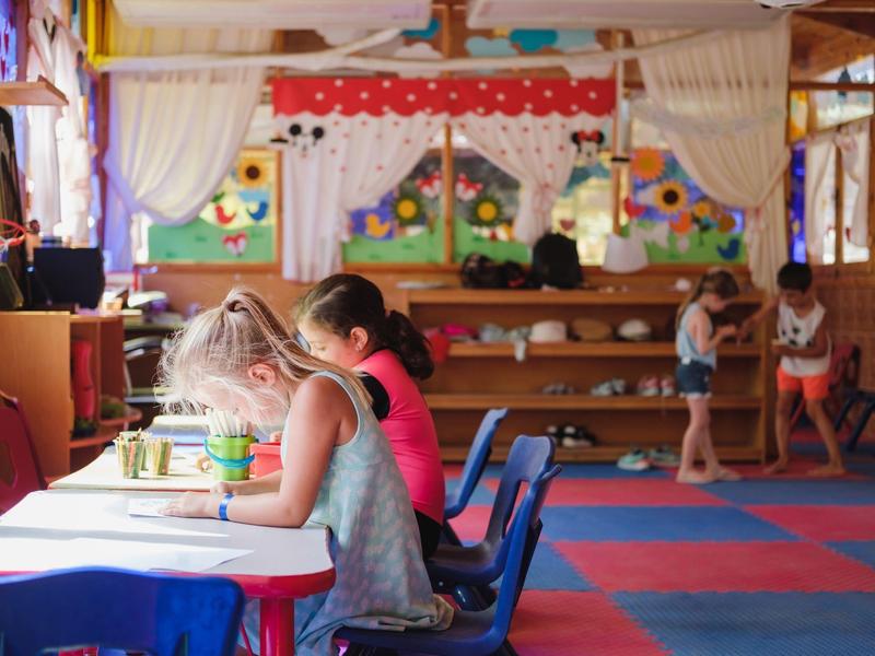 Kinderen zitten aan een tafel in een kleurrijke ruimte en tekenen.