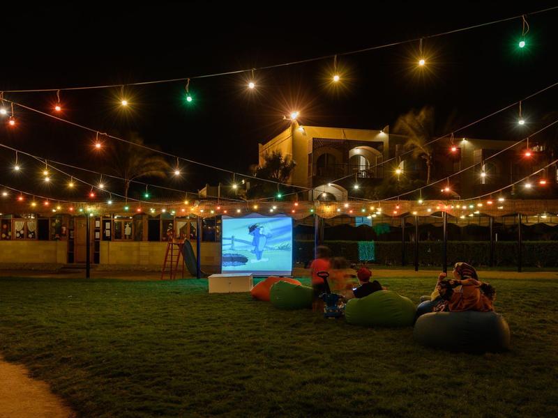 Openlucht bioscoop 's nachts met kleurrijke lichtslingers en gasten op zitzakken op gras.