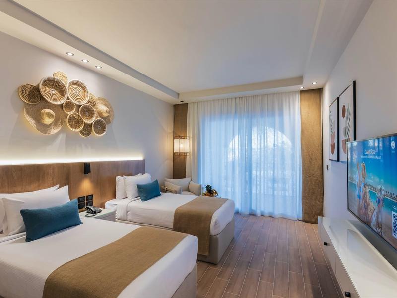 Modern hotelkamer met twee eenpersoonsbedden, neutrale kleuren en balkonzicht.