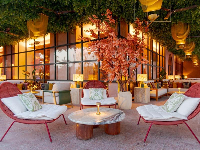 Gezellige lounge met rode stoelen en tafels onder een met planten bedekt dak.