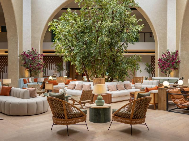 Elegante hotel lobby met ronde sofa's, fauteuils en grote planten onder hoge bogen.