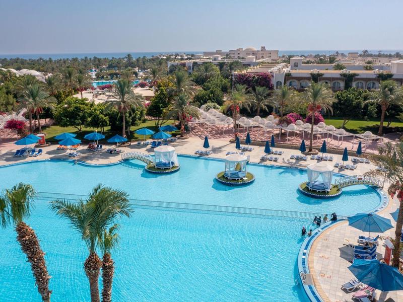 Groot buitenzwembad met parasols, ligstoelen en palmbomen bij een hotelresort.