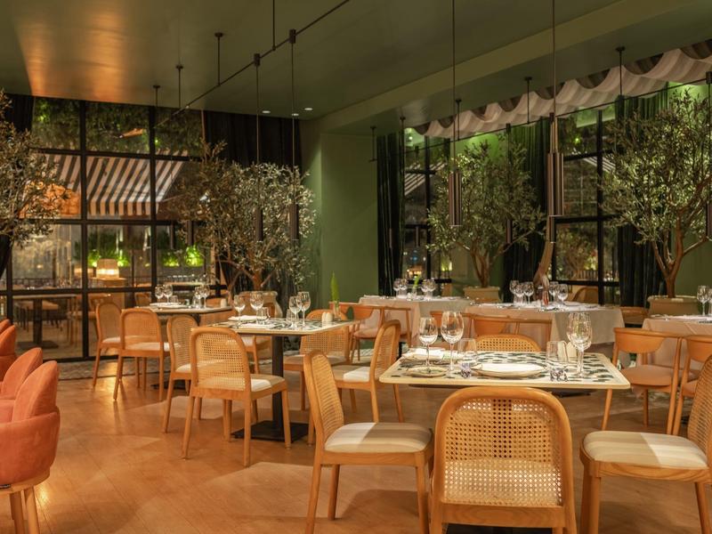 Modern restaurant met houten tafels, rieten stoelen en grote ramen.