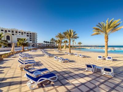 Strand mit Palmen, Sonnenschirmen und blauem Meer unter wolkenlosem Himmel.