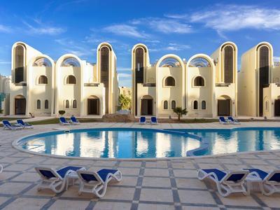 Modernes Hotel mit Pool, Sonnenliegen und architektonischen Bogenfenstern bei blauem Himmel.