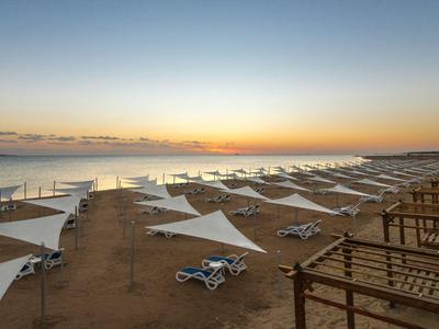 Strand mit weißen Sonnenschirmen, Liegestühlen und einem ruhigen Meer bei Sonnenuntergang.