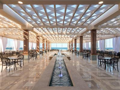 Otwarta przestrzeń hotelowa z stołami, krzesłami, kanałem wodnym i widokiem na morze.