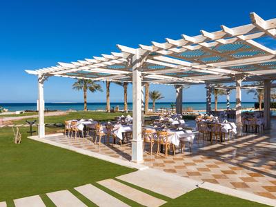 Offener Hotelpatio mit weißen Pergolen und Tischen mit Blick auf das Meer