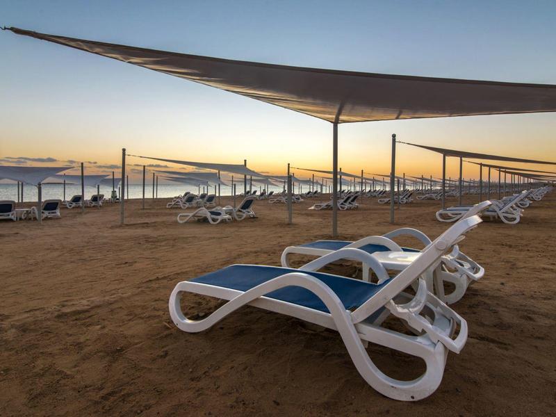 Widok na ośrodek z basenem i ogrodem nad morzem o zachodzie słońca.