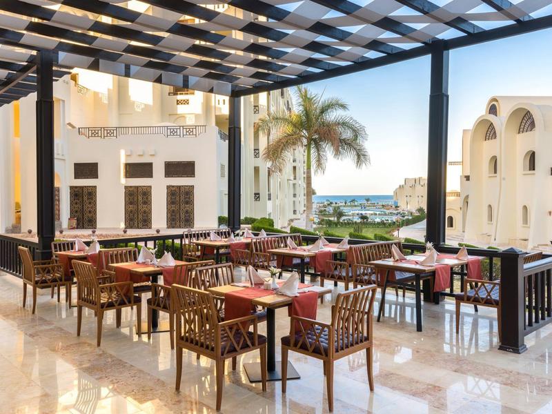 Nowoczesny zewnętrzny obszar hotelu z stołami i krzesłami pod dachem pergoli.