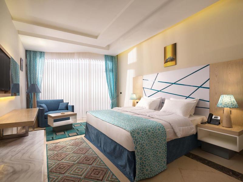 Nowoczesny pokój hotelowy z dużym łóżkiem, miejscem do siedzenia i oknem z niebieskimi zasłonami.